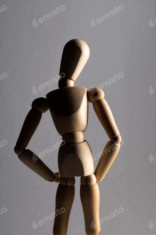 Preview: Vertical closeup shot of a wooden pose doll with its hands on its waist standing in the shade