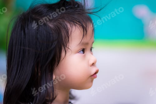 Preview: Portrait side view of Asian cute little girl with curious face in house.
