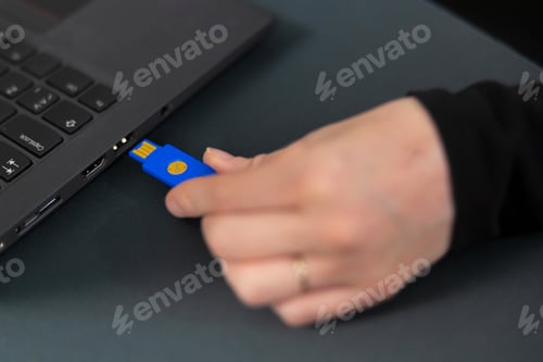 Preview: Female IT security technician in a tech office connects blue USB drive to a laptop