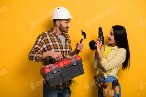 Preview: happy manual workers holding toolbox and electric drill on yellow