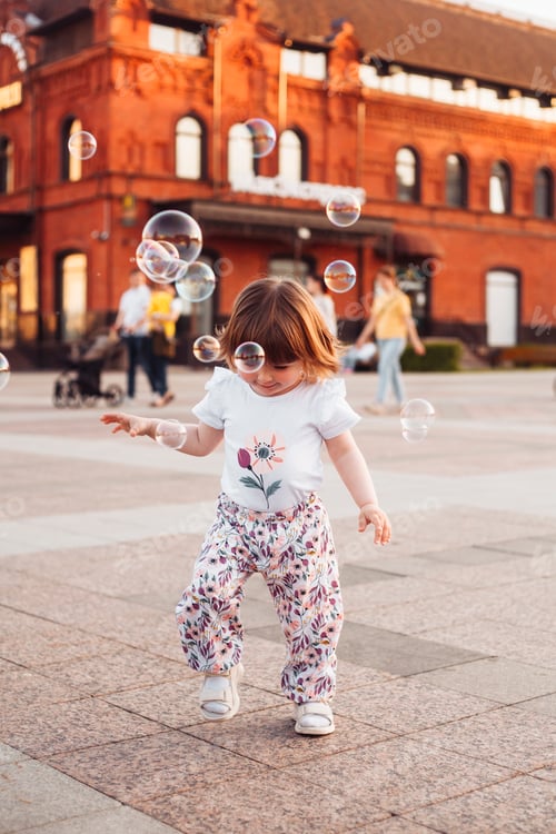 Preview: little girl playing and having fun with soap bubbles on the street in summer at sunset