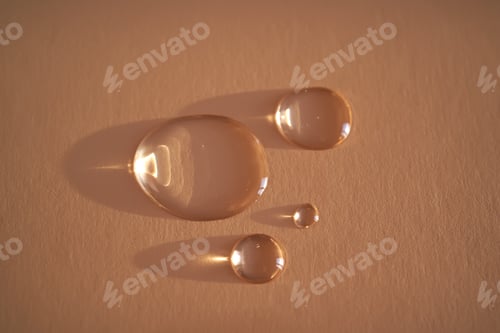 Preview: Beautiful volumetric drops of cosmetic product on a beige background.