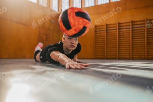 Preview: Woman playing volleyball in a sports hall and sliding on a court to hit a ball