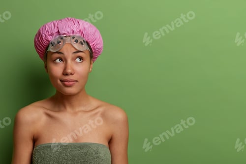 Preview: Indoor shot of pensive dark skinned model going to swimming pool, wears water protective hat, rubber
