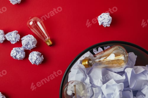 Preview: top view of office trash bin with crumpled papers and vintage incandescent lamps on red tabletop