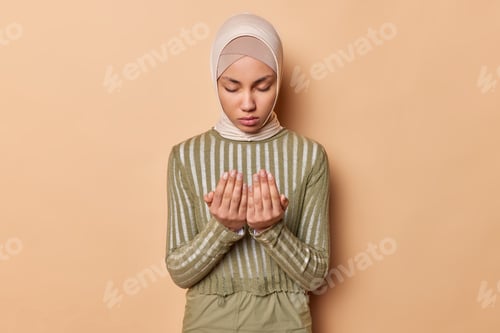 Preview: Muslim woman keeps palms together poses in praying pose keeps eyes closed has calm expression wears