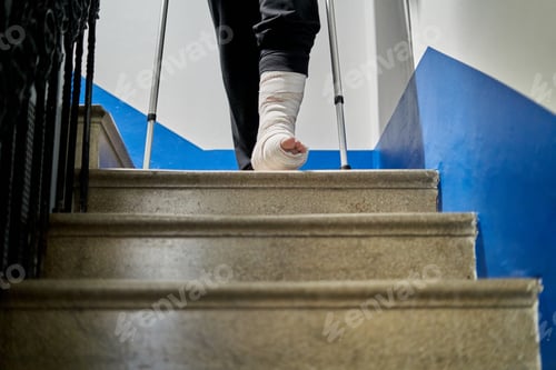Preview: Unrecognizable man with crutches and broken leg walks down the stairs at home