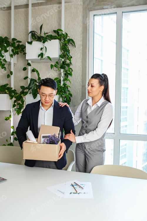 Preview: Colleague seeing off sad fired asian male office worker holding box of his personal stuff.