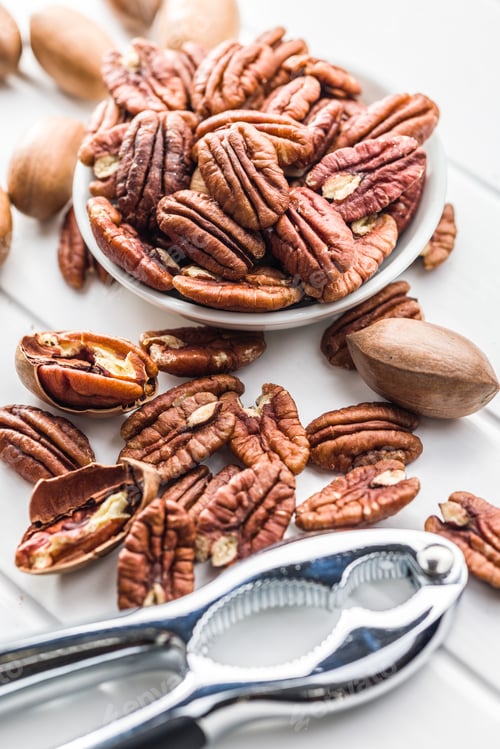 Preview: Peeled pecan nuts in bowl on white table.