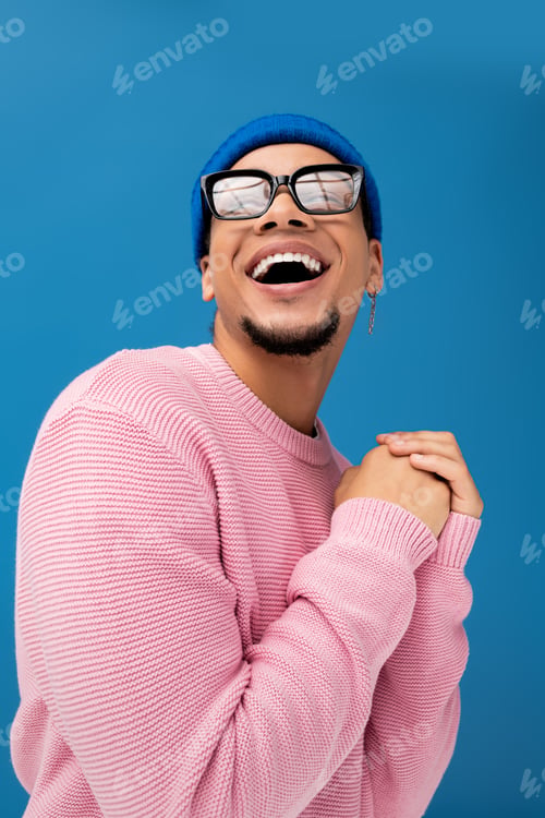 Preview: Charming young man in trendy outfit smiling against a vibrant blue backdrop