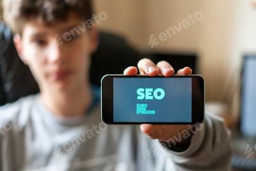 Preview: young male worker holding a smartphone with SEO text design in the office, search engine