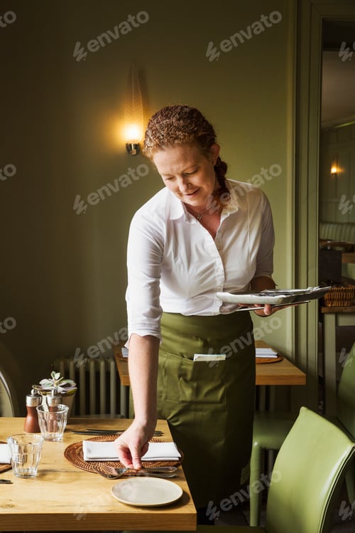 Preview: Woman wearing apron setting table in a restaurant.