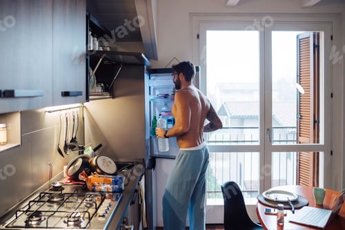 Preview: Mid adult man removing bottled water from fridge