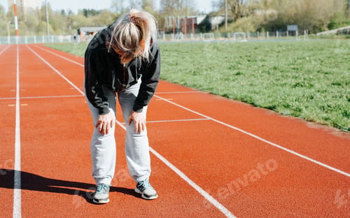 Preview: Tired adult woman while running in stadium outdoors. An unrecognizable overweight woman breathing