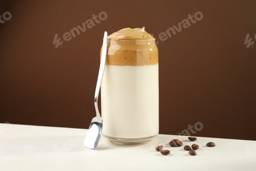 Preview: Delicious dalgona coffee in glass, beans and spoon on white table