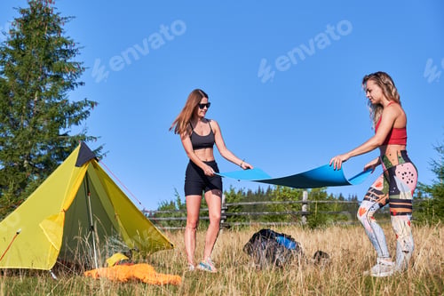 Preview: Two female tourists standing, making campsite in hills.