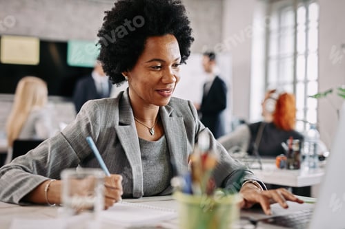 Preview: Smiling African American woman working at her desk in the office.