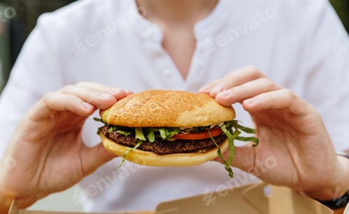 Preview: A young guy holds a burger in his hands while sitting in a cafe.