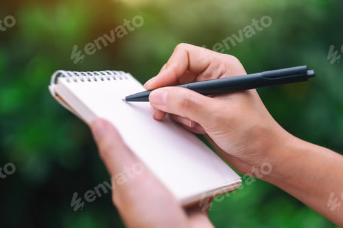 Preview: Closeup image of a woman's hands holding and writing on blank notebook in the outdoors