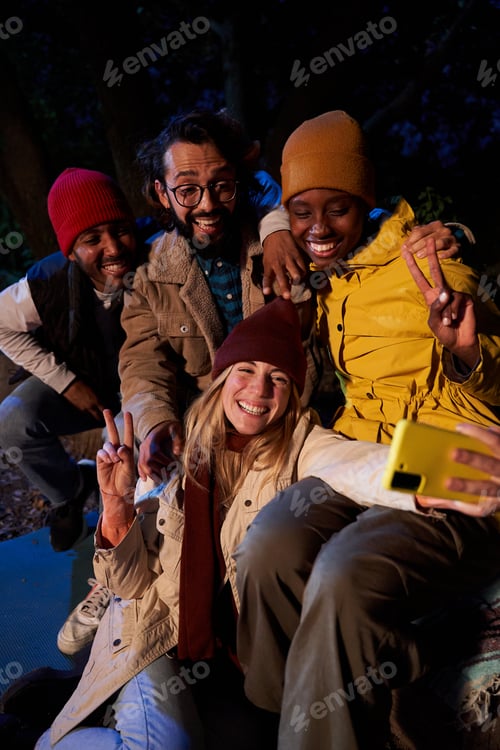 Preview: Cheerful group of multiethnic friends using phone to take a selfie while gathering outdoors at night