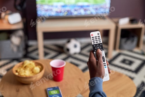 Preview: Close up of man watching football match at home male hand holding TV remote
