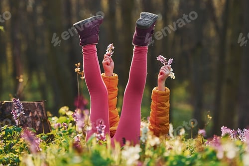 Preview: Happy little girl in casual clothes lying down on ground in spring forest at daytime