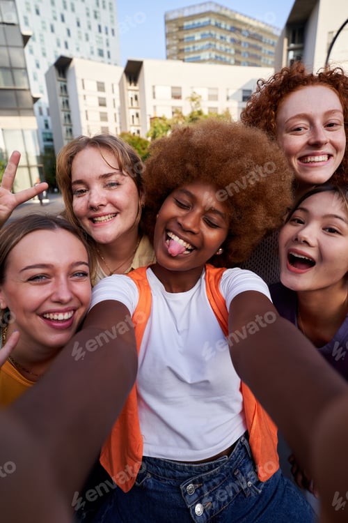 Preview: Happy multiracial female friends taking a selfie with a smartphone outdoors.