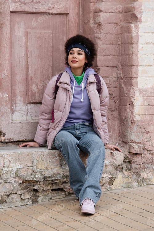 Preview: African american woman sitting on stair near old building