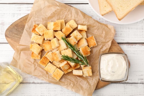 Preview: Delicious crispy croutons with rosemary and sauce on white wooden table, flat lay