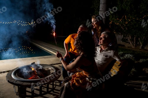 Preview: Mature adult couples watching sparkler by patio fire at night