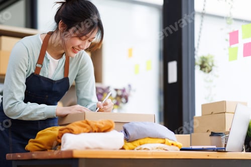 Preview: Startup SME small business entrepreneur of freelance Asian woman wearing apron using laptop and box
