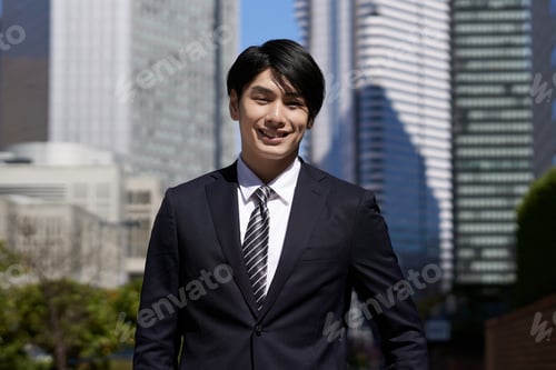 Preview: A smiling Japanese male businessman stands in an office district.