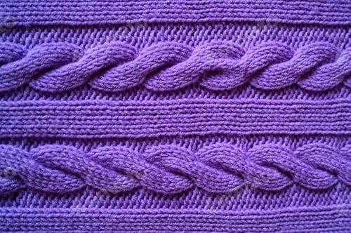 Preview: background of beautiful knitted cozy purple sweater with braided pattern