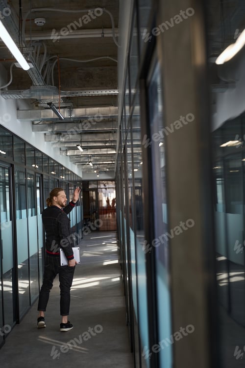 Preview: Attractive male employee waving hand in corridor