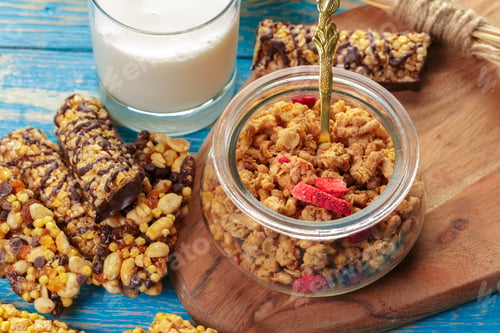 Preview: Granola and snack bars on wooden plate with glass of milk and jar on blue table