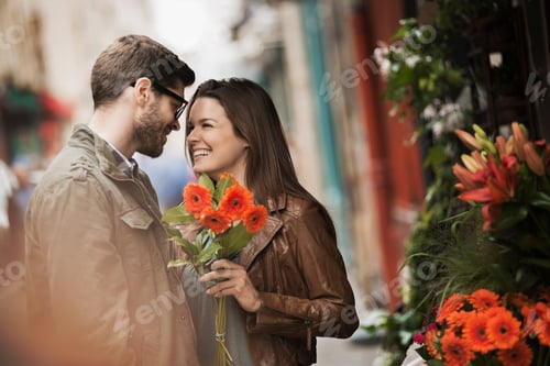 Preview: A man and woman by a flower stall in the city, holding a bunch of bright red flowers.