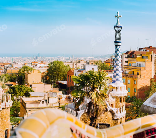 Preview: Porter lodge colorful tower and details of ceramic bench in Park Guell. Warm sunlight on rooftops
