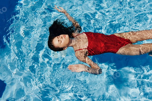 Preview: Young woman in the pool in a red swimsuit with a beautiful smile lying on the water and swimming in