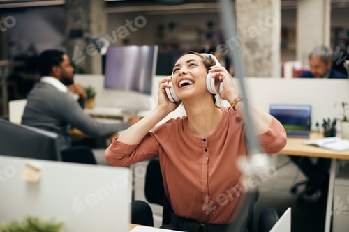 Preview: Carefree businesswoman enjoying in music over headphones in the office.