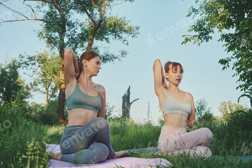 Preview: Personal Yoga trainer teaching young woman or her friend gomukhasana outdoor