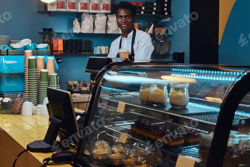 Preview: Portrait of a handsome African barista at counter of a trendy coffee shop.