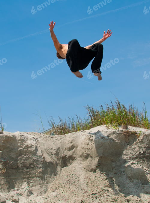 Preview: Male shirtless athlete on the air doing somersault against a clear blue sky