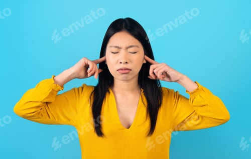 Preview: Asian woman wear casual shirt cover ears with hands fingers