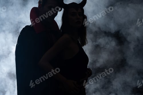 Preview: silhouette of man and woman in halloween costumes standing on black with smoke
