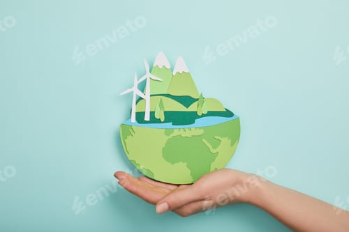 Preview: top view of woman holding paper cut planet with renewable energy sources on turquoise background,