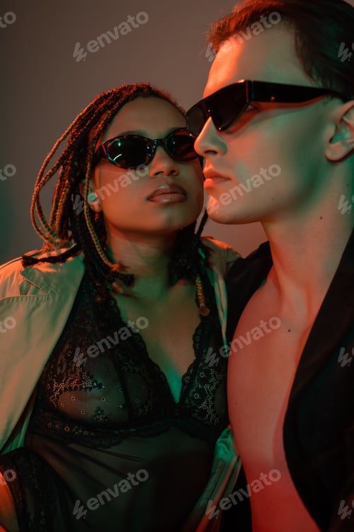 Preview: self-assured man in dark sunglasses near african american woman with dreadlocks, in black lace
