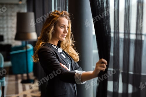 Preview: Pensive young beautiful businesswoman looking through window