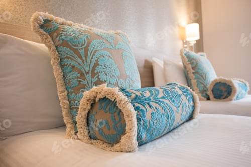 Preview: Shot of two decorative pillows with floral turquoise pattern on white bedsheets in a hotel room
