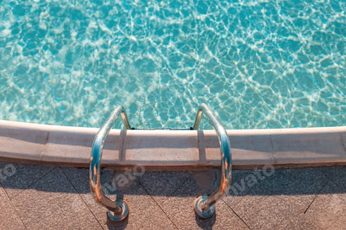 Preview: Beautiful swimming pool with azure blue water and metal descent at sunset, top view.