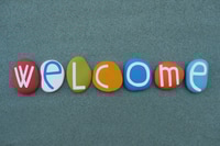 Preview: Welcome, creative word composed with multi colored stone letters over green sand